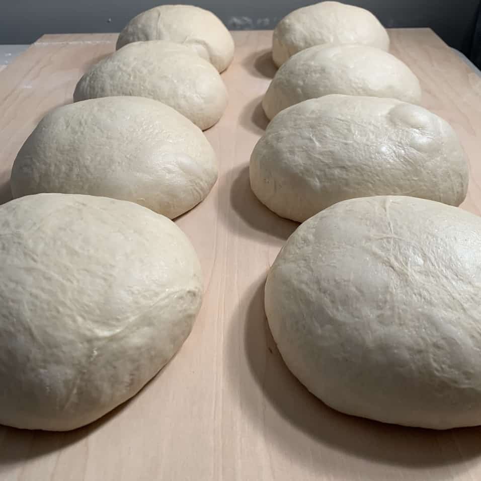 8 loaves of sourdough proofing on table.